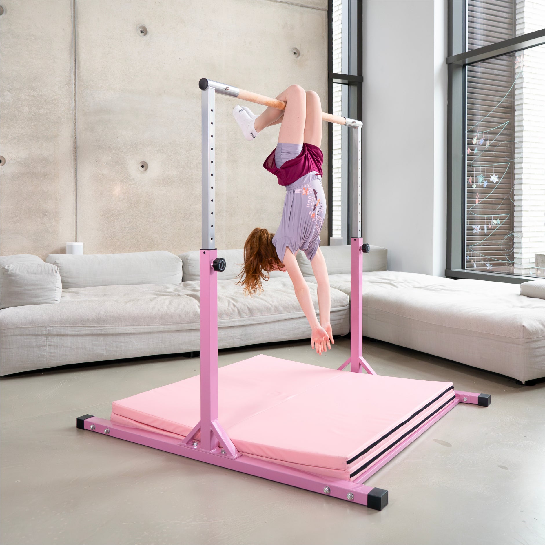 ädchen hängt kopfüber an einem rosa Turnreck auf einer rosa Gymnastikmatte, perfekt für sportliche Aktivitäten in Innenräumen.