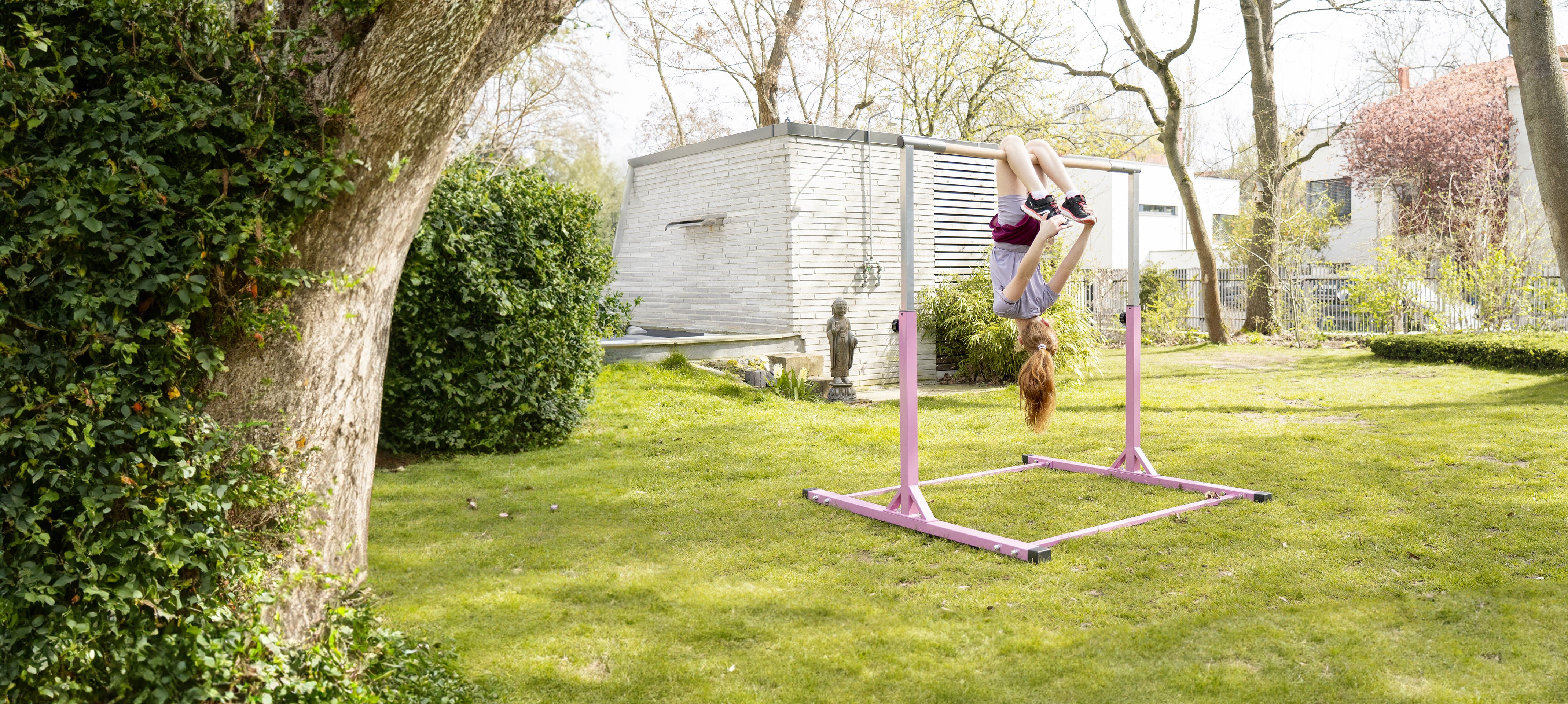 Mädchen turnt kopfüber an einem pinken Turnreck im Garten. Das Outdoor-Turnreck bietet Kindern eine sichere Möglichkeit, aktiv zu sein und motorische Fähigkeiten in der Natur zu fördern.