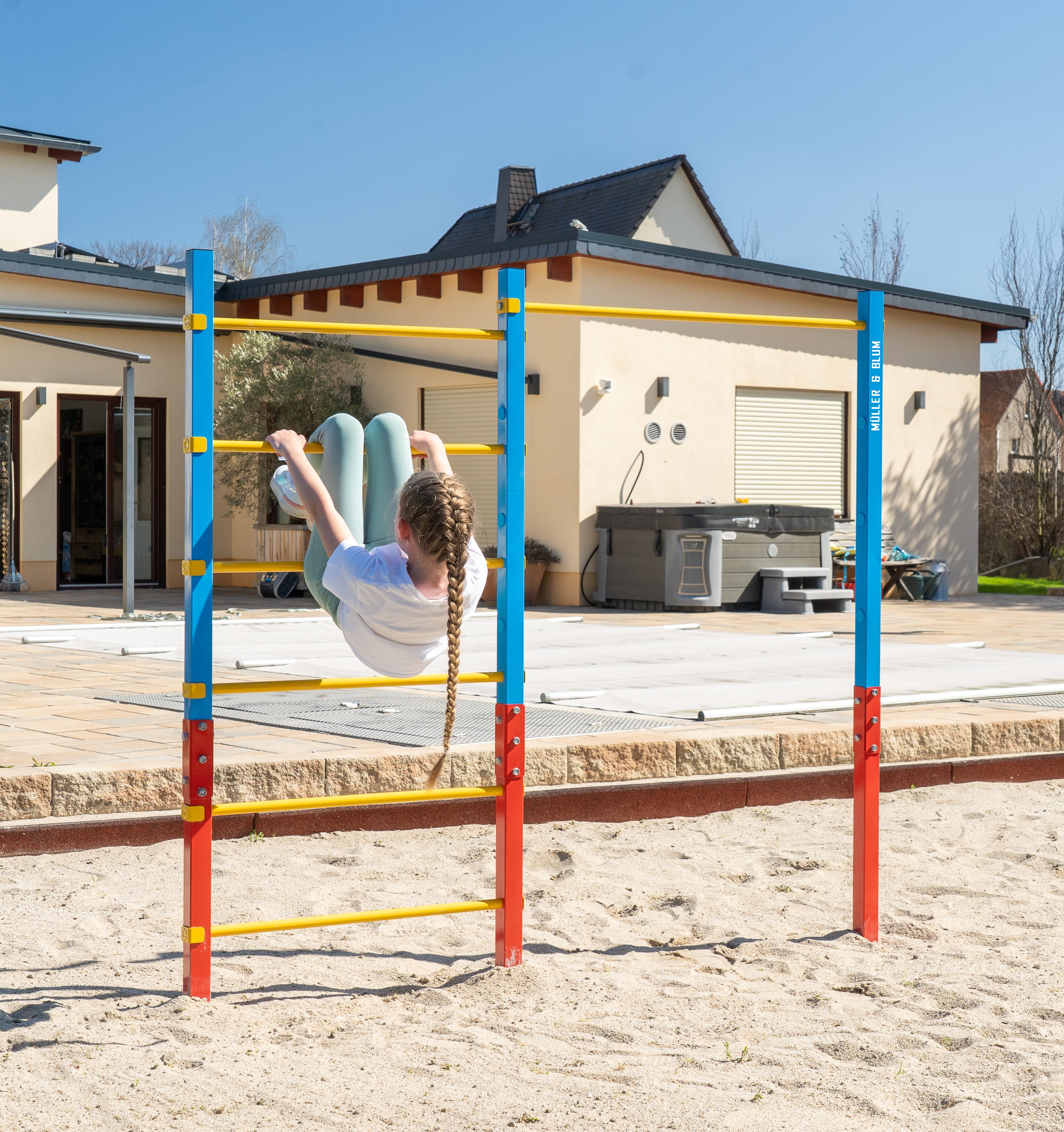 Mädchen turnt fröhlich an einer höhenverstellbaren Reckstange eines Outdoor-Turngeräts im Garten. Die Aufbauanleitung zeigt die einfache Montage mit Bodenanker und Beton für das Klettergerüst für Kinder.