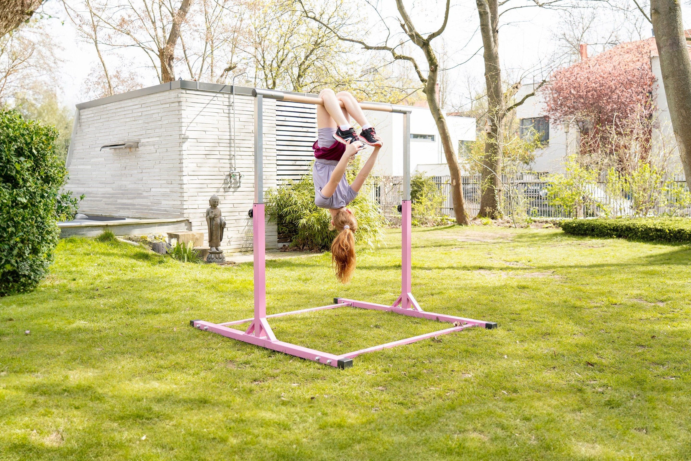 Mädchen turnt kopfüber an einem pinken Turnreck im Garten. Das Outdoor-Turnreck bietet Kindern eine sichere Möglichkeit, aktiv zu sein und motorische Fähigkeiten in der Natur zu fördern.